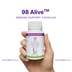 Hand holding a bottle of 98 Alive immune support capsules against a white background